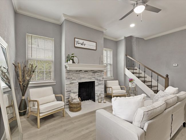 Living area with light wood finished floors, a ceiling fan, ornamental molding, stairs, and a fireplace with raised hearth | Image 9