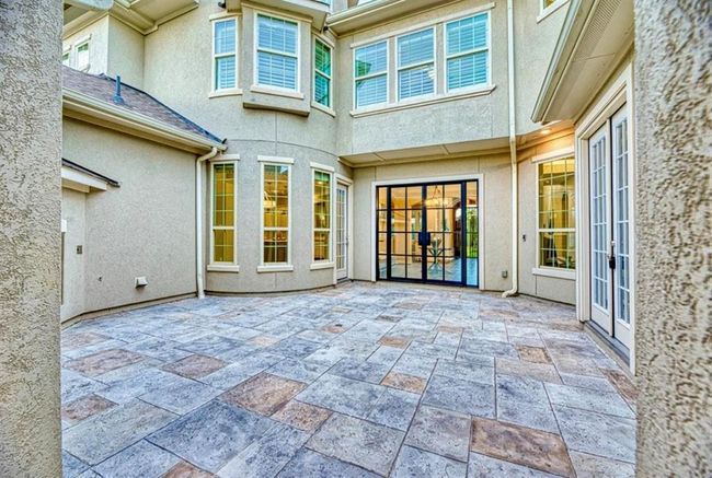 This photo showcases a spacious, tiled courtyard with large windows and French doors, providing ample natural light and a seamless indoor-outdoor flow. Ideal for entertaining or relaxing, the area is surrounded by a light-colored exterior, offering a modern and inviting atmosphere. | Image 6
