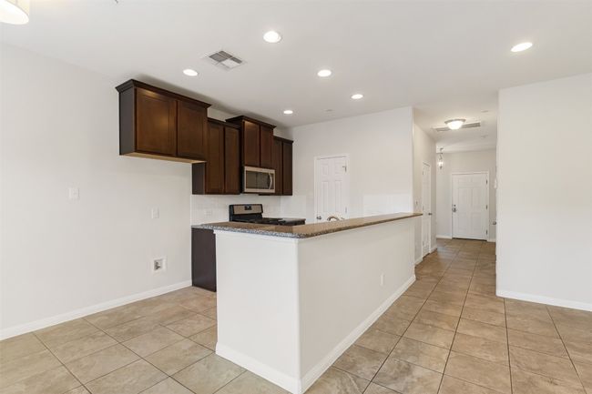 Kitchen featuring stainless steel appliances, light tile patterned floors, recessed lighting, dark brown cabinetry, and dark stone countertops | Image 9