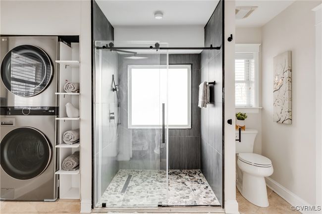 Bathroom featuring a stall shower, toilet, visible vents, and stacked washer and clothes dryer | Image 40