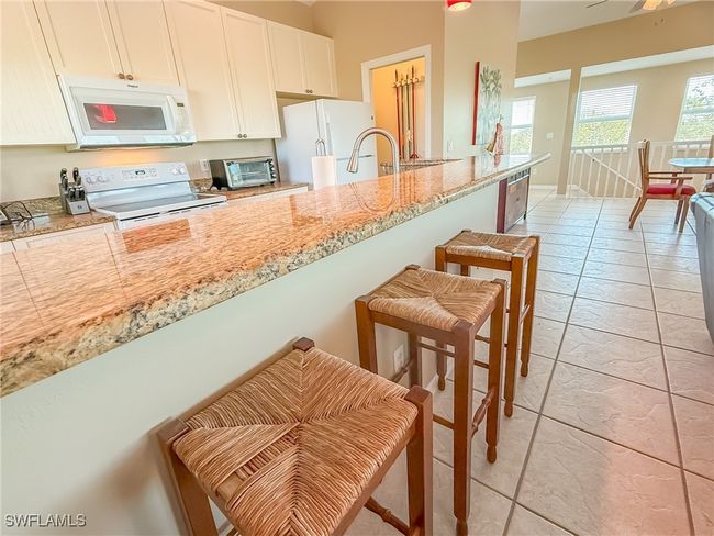 Kitchen with light tile patterned floors, light stone counters, white appliances, white cabinetry, and a kitchen breakfast bar | Image 17