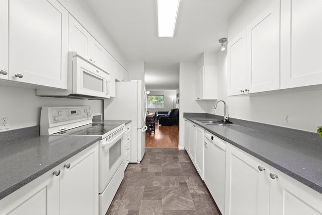 Kitchen featuring white appliances, white cabinetry, a sink, and dark stone counters | Image 10