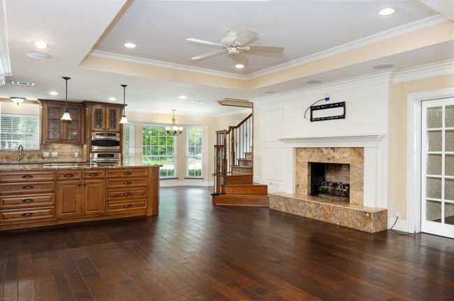 Kitchen featuring brown cabinets, dark wood-style flooring, light stone countertops, a ceiling fan, and glass insert cabinets | Image 11
