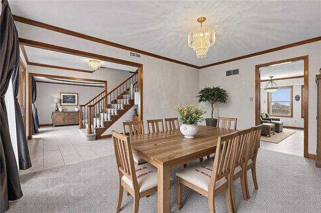 Dining area with a chandelier, light carpet, visible vents, ornamental molding, and stairway | Image 5