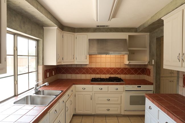 Kitchen with oven, exhaust hood, tile counters, gas cooktop, and backsplash | Image 30