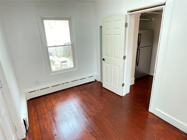 Unfurnished bedroom with freestanding refrigerator, baseboard heating, and dark wood finished floors | Image 14