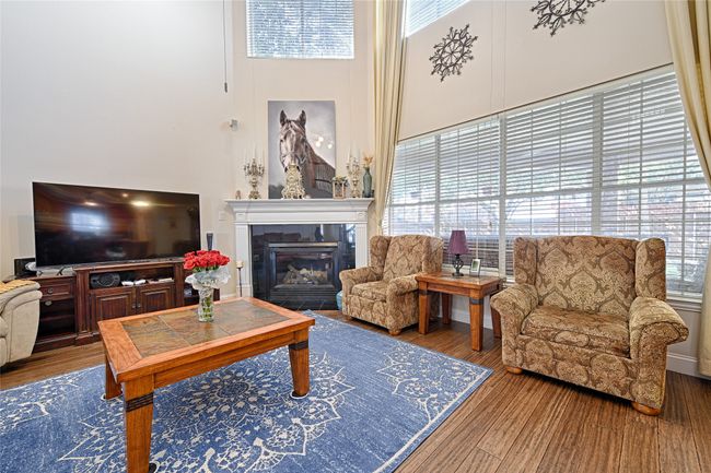 Living area featuring a high ceiling, a tiled fireplace, and wood finished floors | Image 23