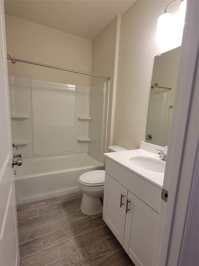 Full bathroom featuring toilet, wood finish floors, vanity, shower / bathing tub combination, and a textured wall | Image 13
