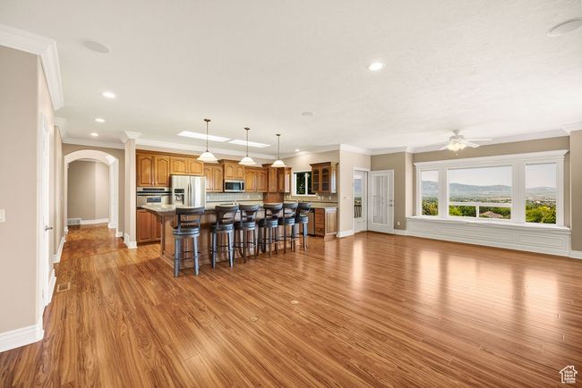Kitchen with stainless steel appliances, a breakfast bar, a kitchen island, brown cabinets, and ornamental molding | Image 12
