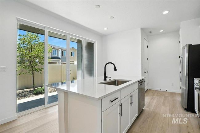 Kitchen with appliances with stainless steel finishes, light wood finished floors, an island with sink, light countertops, and white cabinetry | Image 12