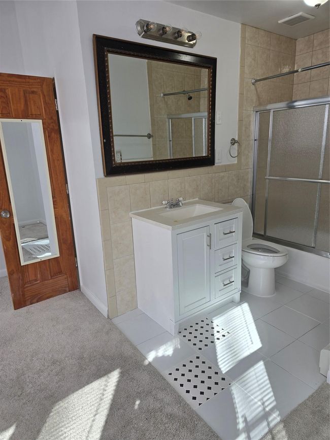Bathroom with tile patterned flooring, toilet, shower / bath combination with glass door, vanity, and tile walls | Image 19
