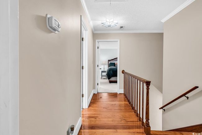 Hallway with an upstairs landing, light wood-style flooring, crown molding, attic access, and a textured ceiling | Image 22