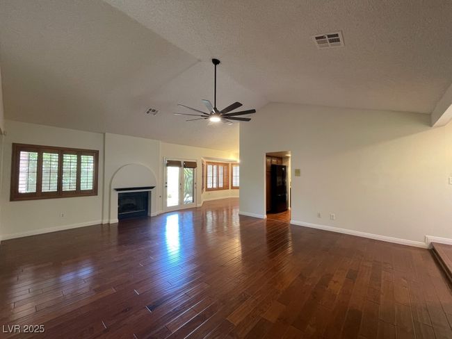 Unfurnished living room with ceiling fan, dark wood-type flooring, healthy amount of natural light, lofted ceiling, and a textured ceiling | Image 9