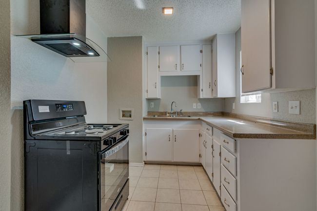 Kitchen with a sink, black gas stove, wall chimney range hood, a textured ceiling, and white cabinets | Image 10