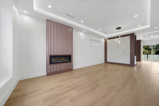 Unfurnished living room with a raised ceiling, light wood-style floors, recessed lighting, and a large fireplace | Image 10