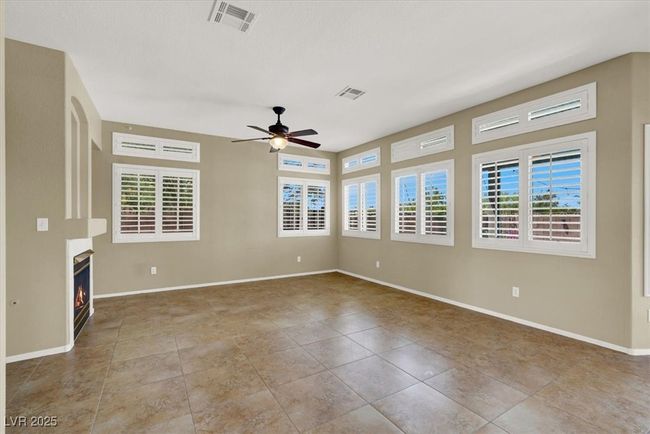 Tiled spare room with a ceiling fan and a warm lit fireplace | Image 10