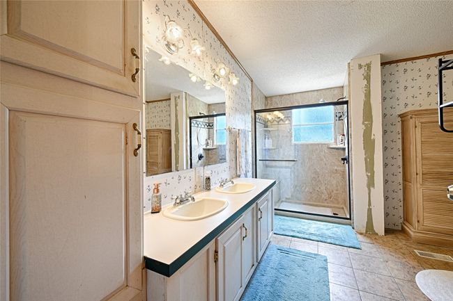Bathroom featuring wallpapered walls, a shower stall, double vanity, a textured ceiling, and light tile patterned floors | Image 13