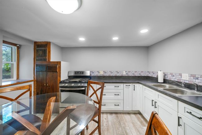 Kitchen with a sink, stainless steel gas range oven, dark countertops, light wood-style floors, and white cabinetry | Image 5