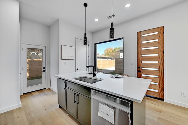 Kitchen featuring dishwasher, a kitchen island with sink, sink, decorative light fixtures, and light wood-type flooring | Image 11