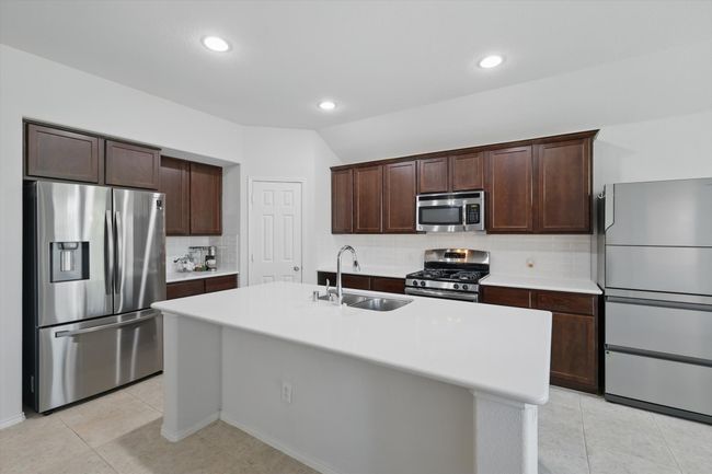 Kitchen with a sink, dark brown cabinets, backsplash, light countertops, and appliances with stainless steel finishes | Image 24