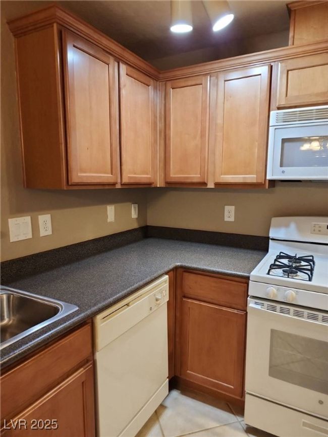 Kitchen with light tile patterned flooring, dark countertops, white appliances, and a sink | Image 7