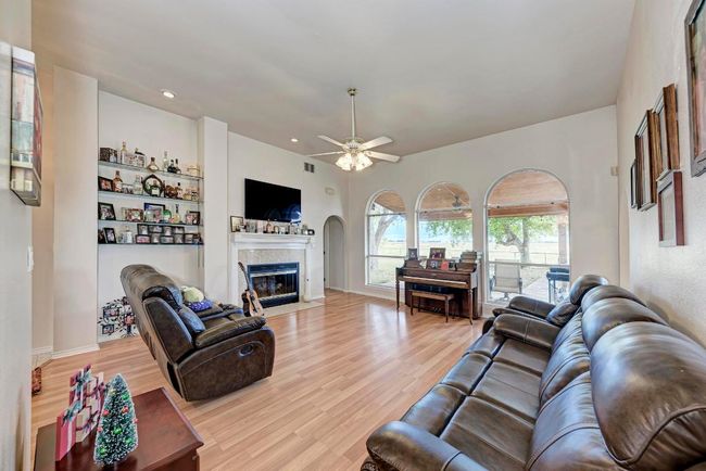 Living area featuring light wood finished floors, a ceiling fan, a fireplace with flush hearth, and recessed lighting | Image 11