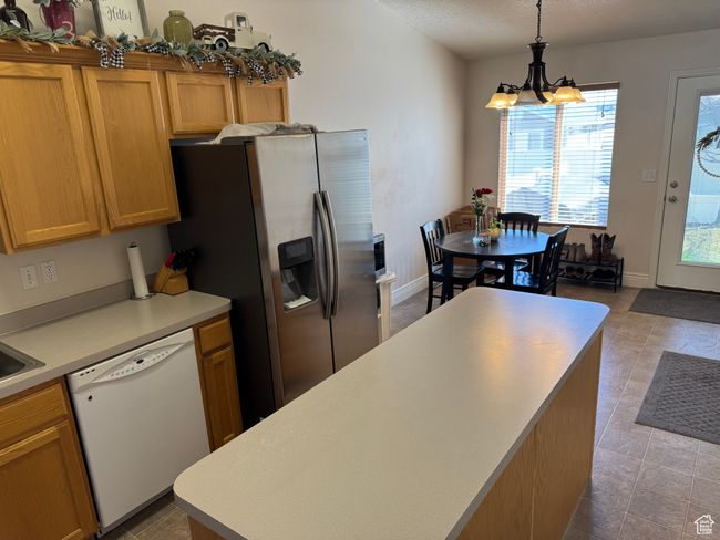 Kitchen featuring light countertops, a chandelier, stainless steel fridge with ice dispenser, pendant lighting, and white dishwasher | Image 5