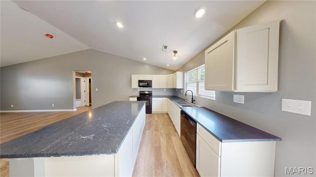 Kitchen featuring black appliances, a sink, light wood-style flooring, lofted ceiling, and a kitchen island | Image 11