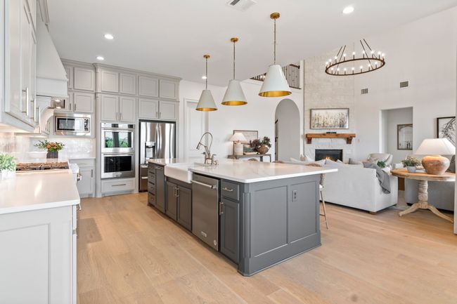 Kitchen with gray cabinetry, pendant lighting, appliances with stainless steel finishes, light wood-type flooring, and arched walkways | Image 13