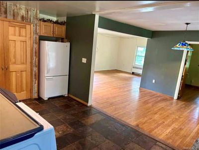 Kitchen featuring dark wood-type flooring, light brown cabinetry, white refrigerator, and radiator heating unit | Image 2