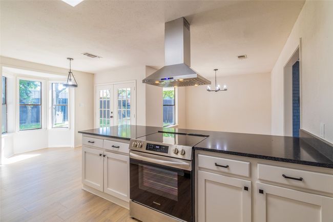 Kitchen featuring light wood finished floors, white cabinets, island exhaust hood, stainless steel electric range oven, and visible vents | Image 6