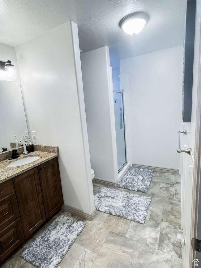 Full bath with a textured ceiling, a stall shower, vanity, toilet, and baseboards | Image 12
