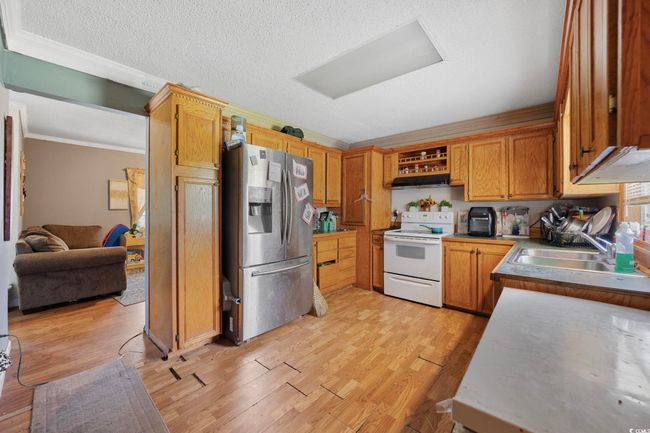 Kitchen featuring stainless steel fridge, white electric stove, crown molding, light wood finished floors, and under cabinet range hood | Image 10