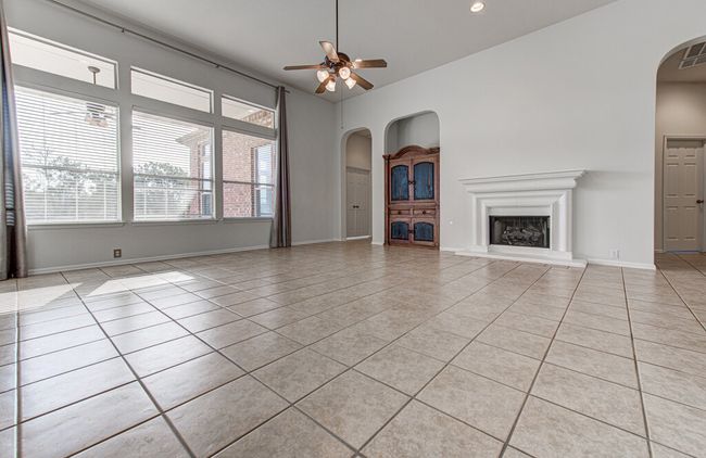 Unfurnished living room featuring a fireplace with raised hearth, baseboards, ceiling fan, light tile patterned floors, and arched walkways | Image 10