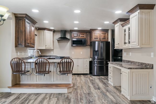 Kitchen featuring light wood finished floors, stainless steel appliances, a peninsula, wall chimney range hood, and stacked washer / dryer | Image 9