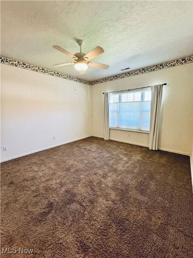 Spare room featuring dark carpet, a textured ceiling, visible vents, and a ceiling fan | Image 29