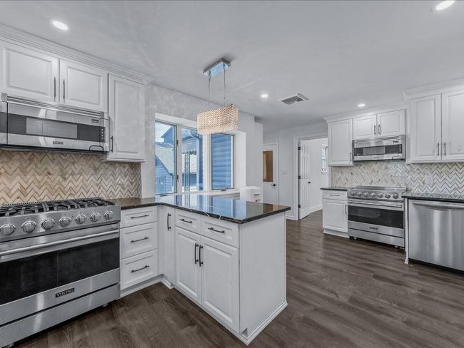Kitchen featuring appliances with stainless steel finishes, a peninsula, white cabinets, backsplash, and dark wood-style flooring | Image 9