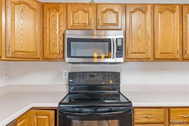 Kitchen with electric range, stainless steel microwave, light countertops, and brown cabinets | Image 8