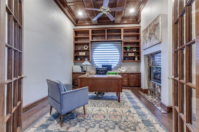 To the left of the foyer is the private office, where you can quietly work behind the glassed double doors. A warm fireplace and beautifully crafted ceiling millwork create a handsome space, and built-in cabinets & shelving surround the circular window and custom shades. | Image 9