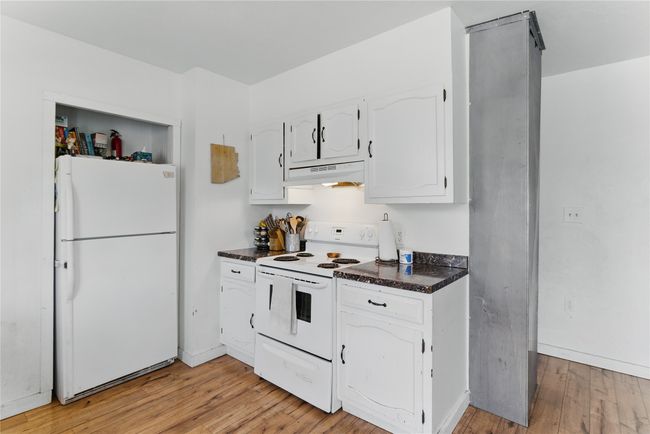 Kitchen featuring dark countertops, white appliances, light wood-type flooring, white cabinetry, and under cabinet range hood | Image 15