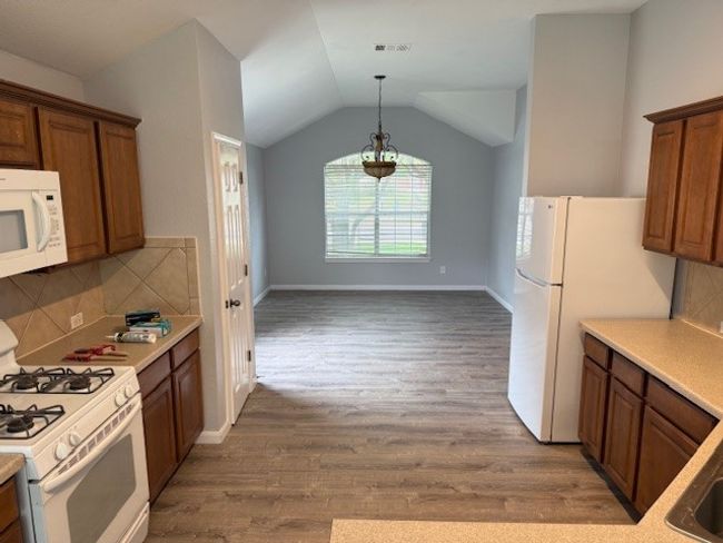 Kitchen featuring white appliances, brown cabinetry, wood finished floors, light countertops, and lofted ceiling | Image 7