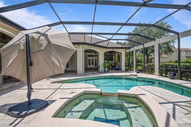 This resort-style pool and spa area offers a tranquil escape with elegant curves, sun shelf, and shaded lounging—all enclosed within a private, screened-in oasis. | Image 29