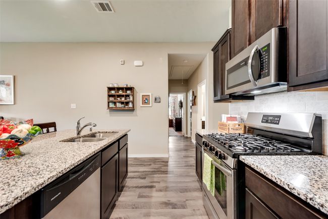 Kitchen featuring appliances with stainless steel finishes, light wood-style floors, dark brown cabinetry, light stone counters, and backsplash | Image 11