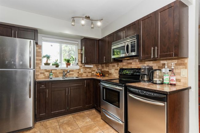 Kitchen featuring stainless steel appliances, dark brown cabinets, decorative backsplash, and light tile patterned flooring | Image 9