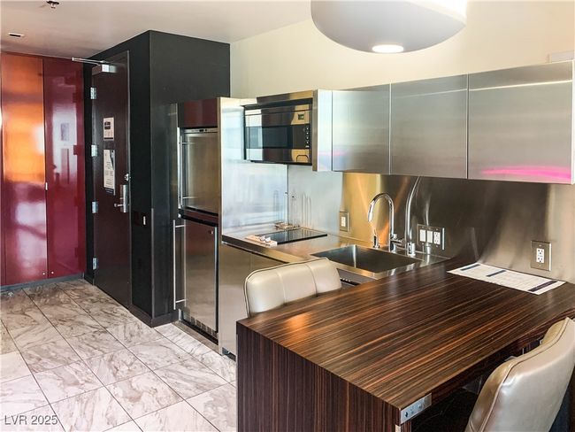 Kitchen featuring stainless steel microwave, light marble finish floors, black electric stovetop, and dark countertops | Image 5