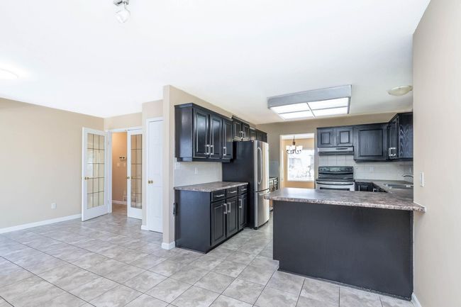 Kitchen featuring a sink, freestanding refrigerator, tasteful backsplash, under cabinet range hood, and range with electric cooktop | Image 12