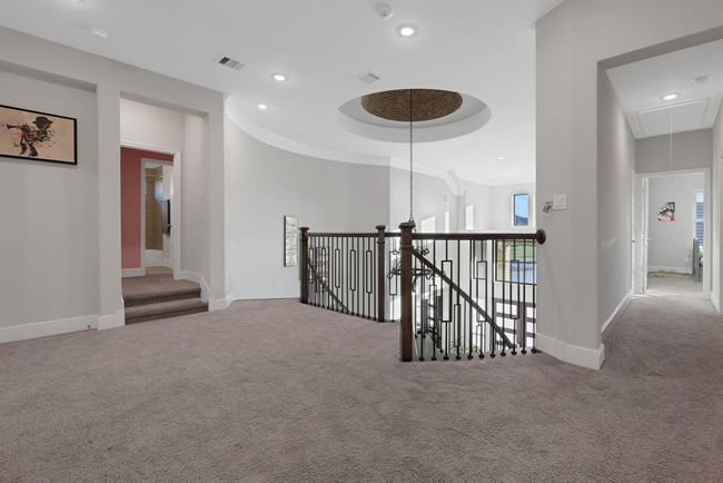The spacious, upstairs landing area with a modern upgraded railing overlooking the staircase and living area below. The space features recessed lighting, multiple doorways leading to other rooms, and a large window providing natural light. | Image 36
