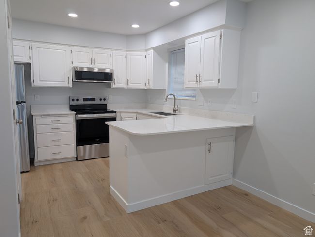 Kitchen with brand new stainless steel appliances, white cabinetry, light countertops, and light wood-style floors | Image 5