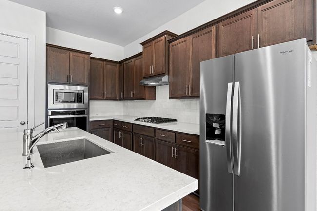 Kitchen featuring stainless steel appliances, a sink, under cabinet range hood, decorative backsplash, and dark brown cabinetry | Image 13
