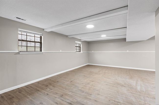 Basement featuring baseboards, visible vents, wood finished floors, and a healthy amount of sunlight | Image 23